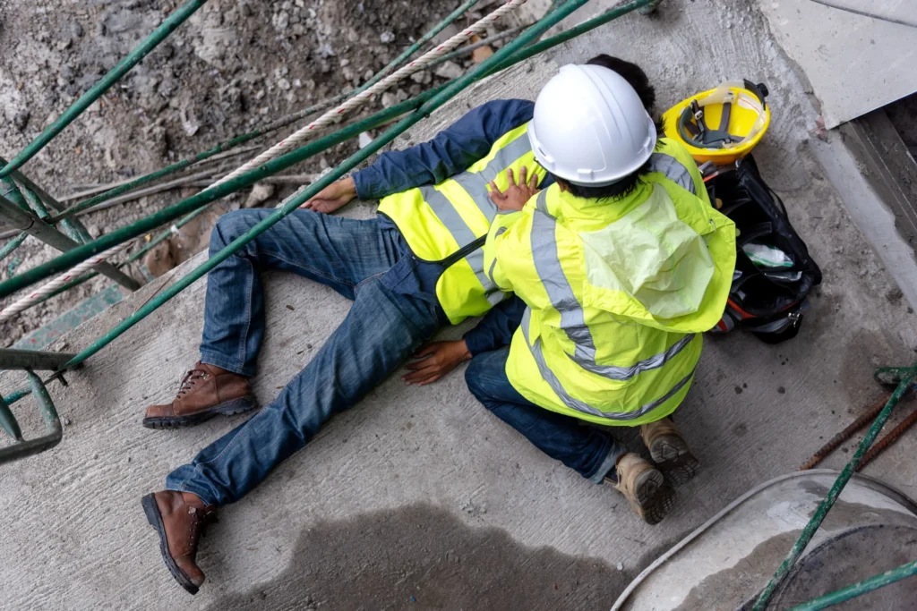 A man fallen on the ground and another worker checking on him.