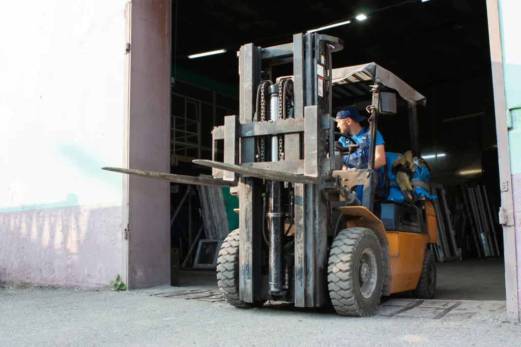 Man driving a forklift outside of a warehouse door.