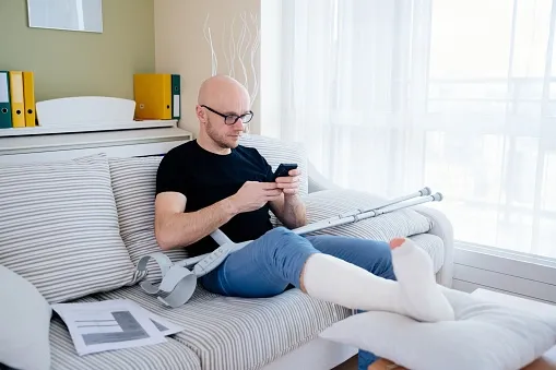 An injured man on the couch on his phone.