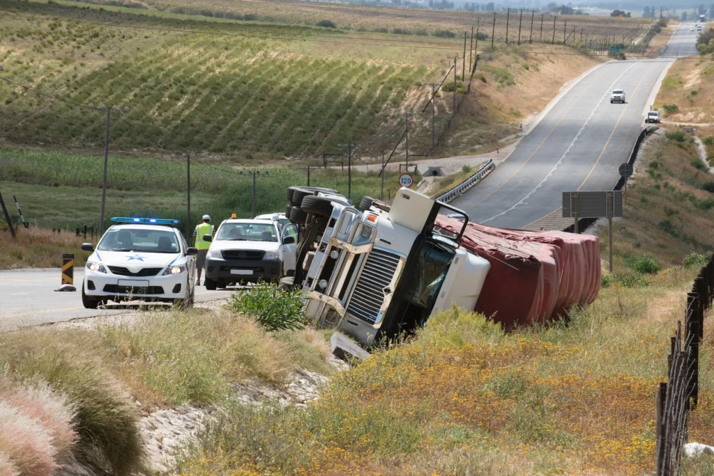 A 18-wheeler truck turned over on the side of the highway.