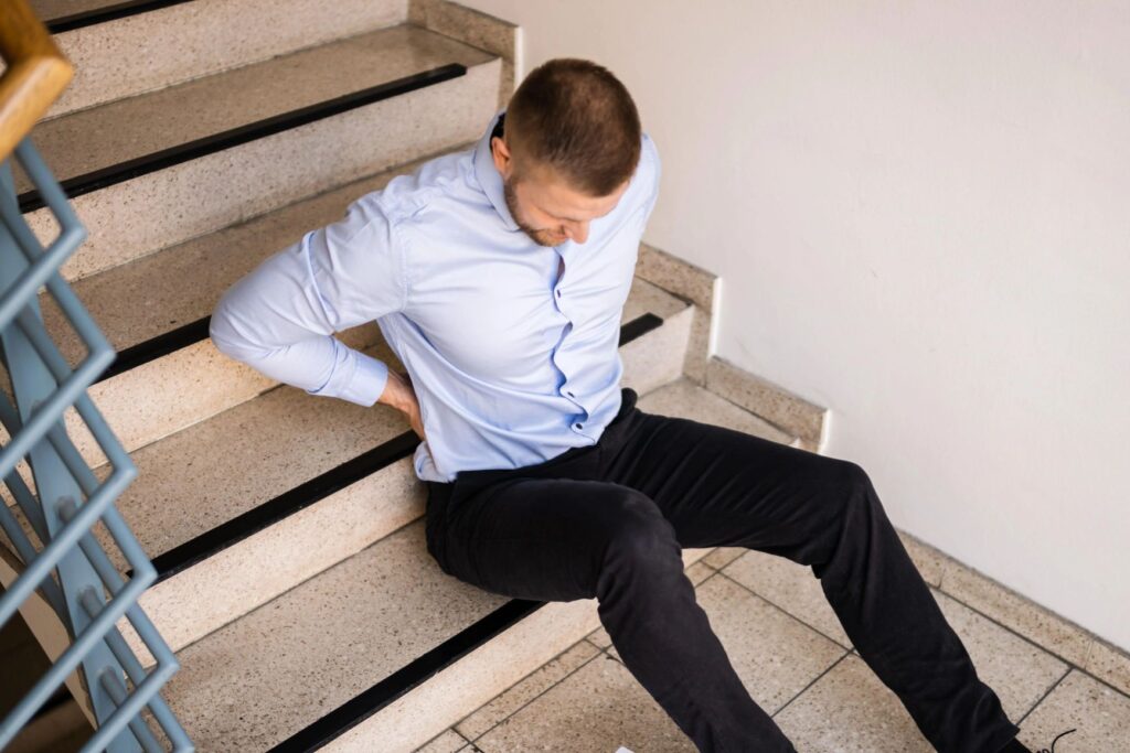 A guy hurt, holding his back while sitting on the stairs.