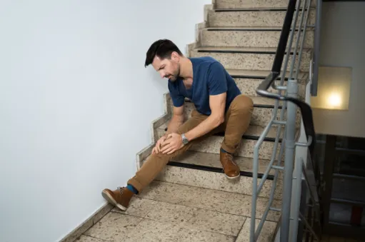 A hurt guy on stairs holding his kneecap.