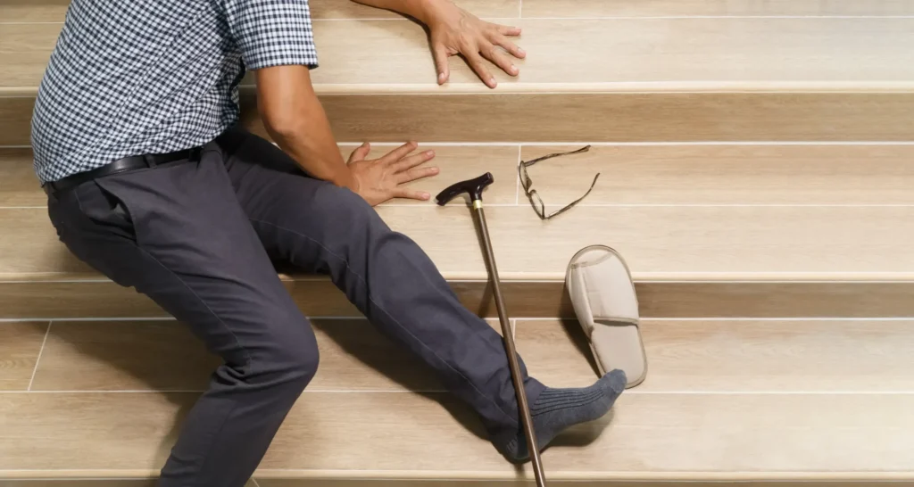 Man who has fallen on indoor stairs with a cane, slipper, and broken glasses nearby, illustrating a slip and fall accident scenario.